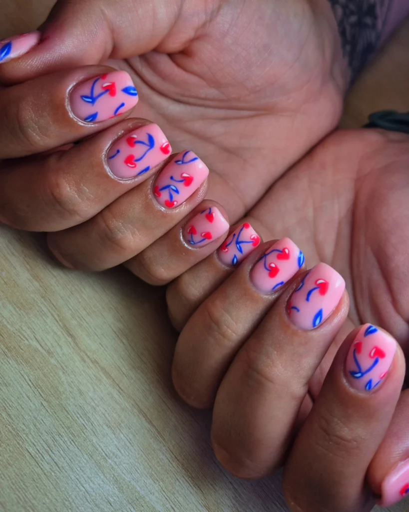 Colorful nail art with blue and red heart designs on short manicured nails.