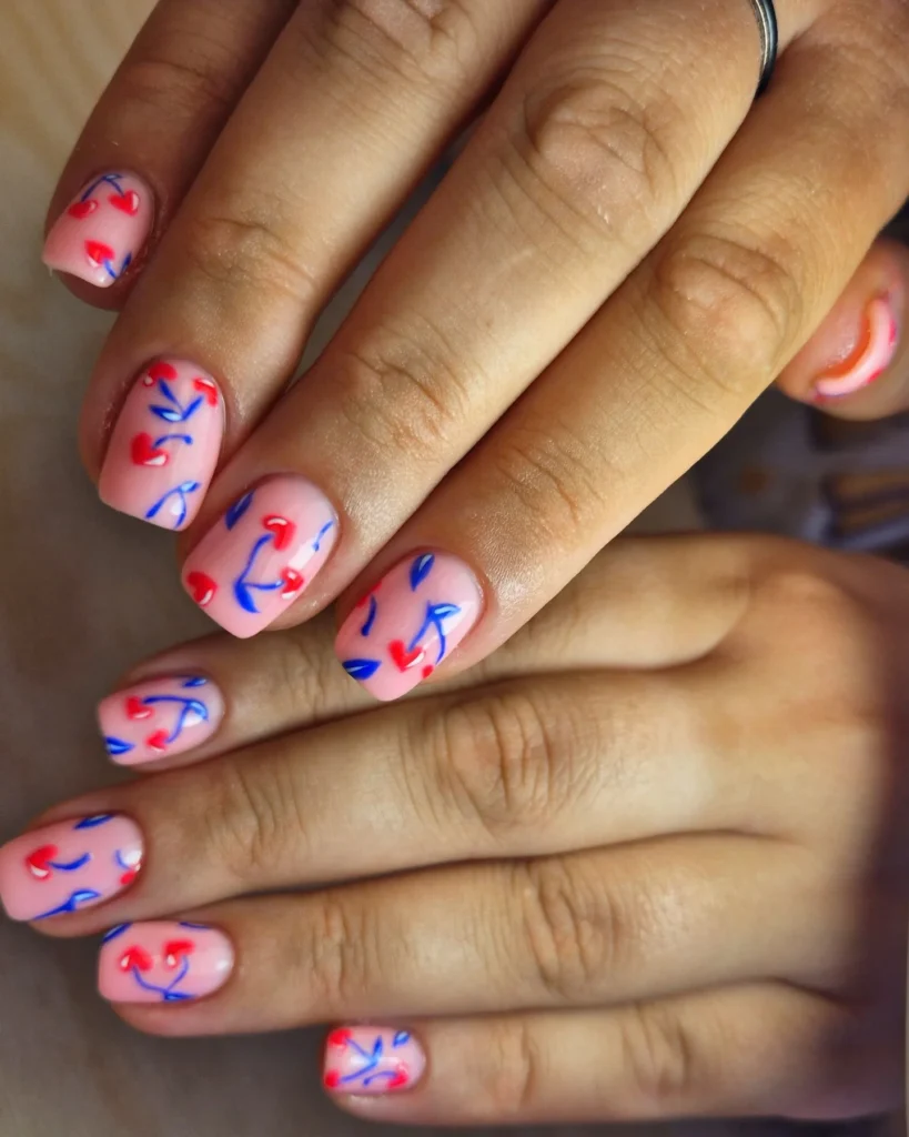 Colorful abstract nail art with red and blue designs on nude polish. Manicure showing hand with vibrant patterns.