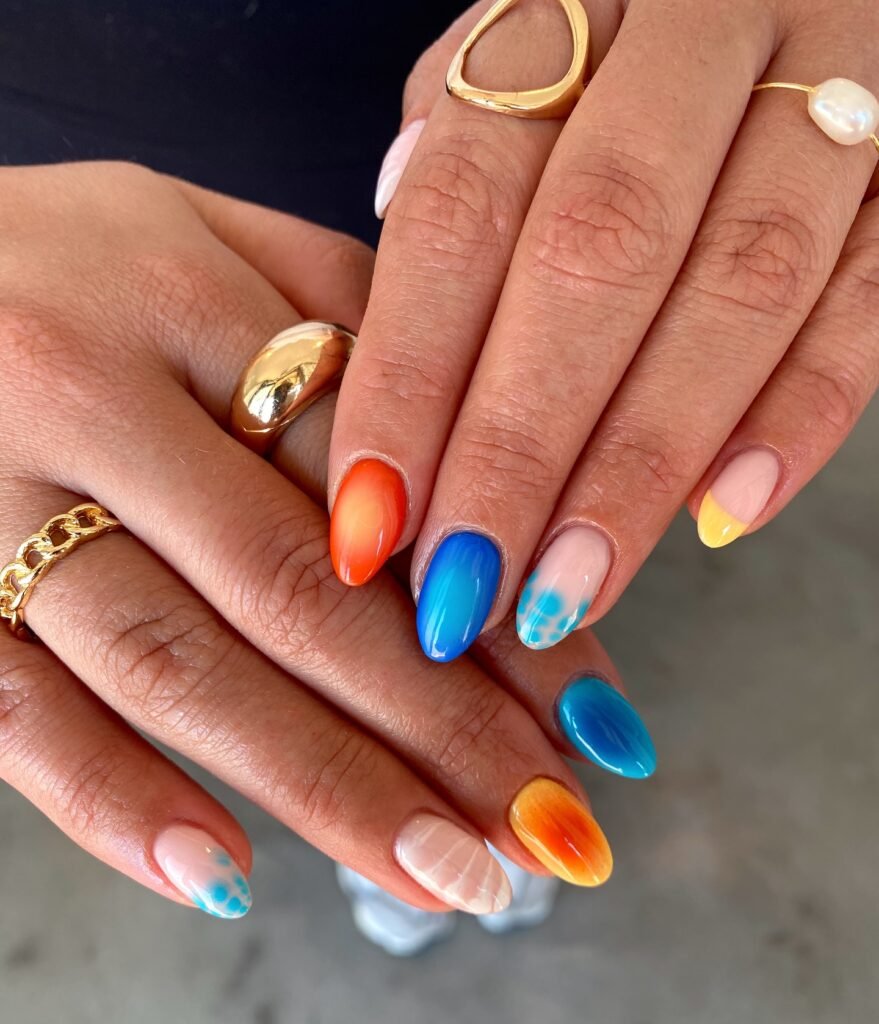Colorful ombre nail art on manicured hands with gold rings, showcasing vibrant blue and orange designs.