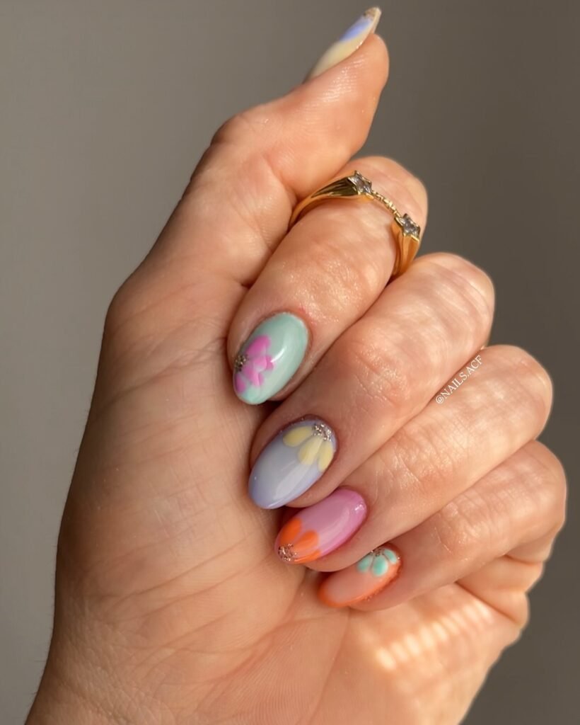 Colorful floral nail art on manicured hand with gold ring in natural light.