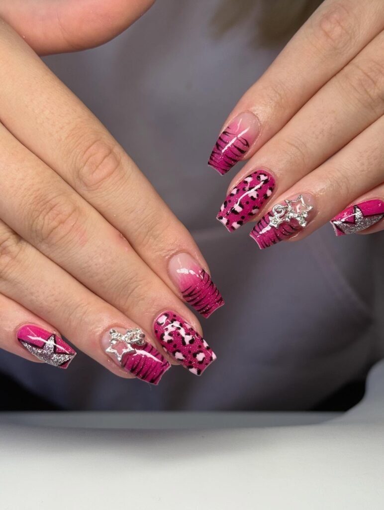 Pink and black nail art with glitter and star accents on long, manicured nails.