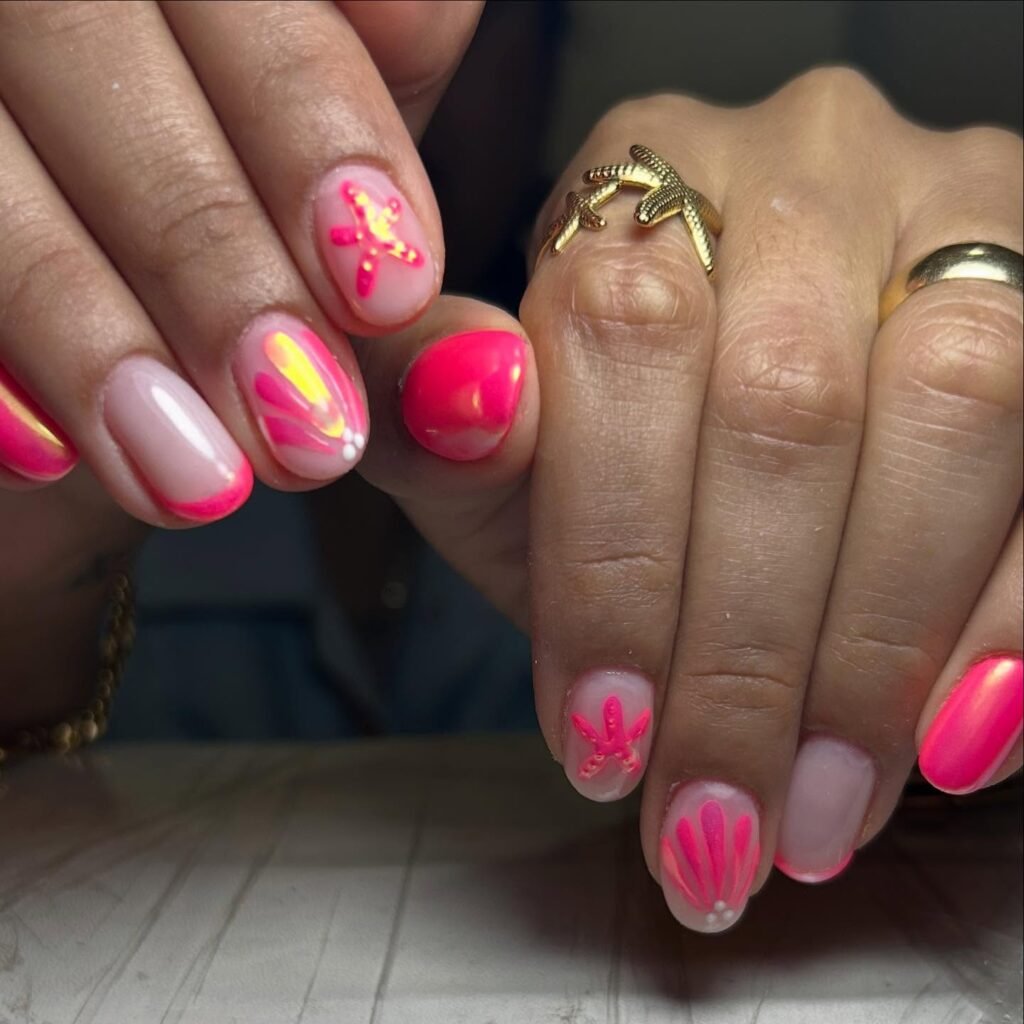Vibrant nail art with pink and orange gradient and starfish designs, complemented by gold starfish rings.