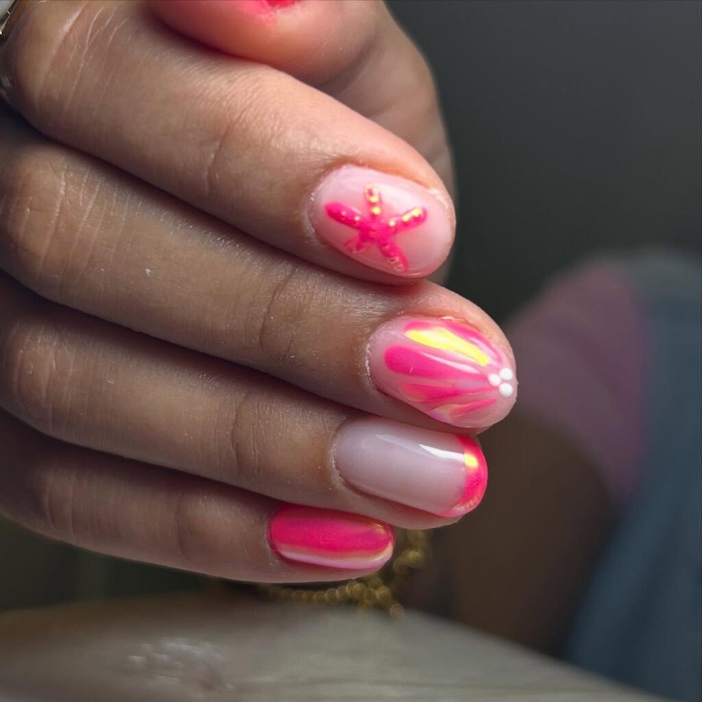 Close-up of a hand with vibrant pink and orange nail art featuring star and swirl designs.