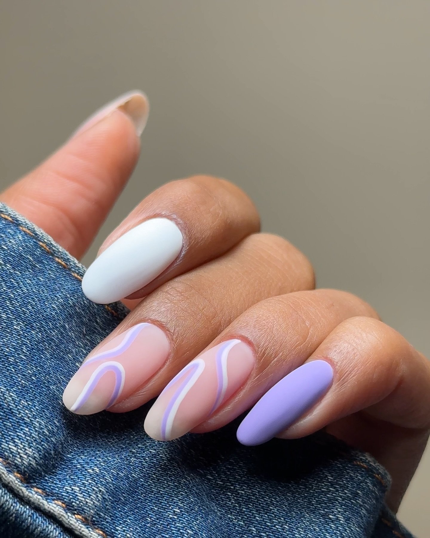 Stylish pastel nail art with white, purple, and wavy design, held against a denim jacket.
