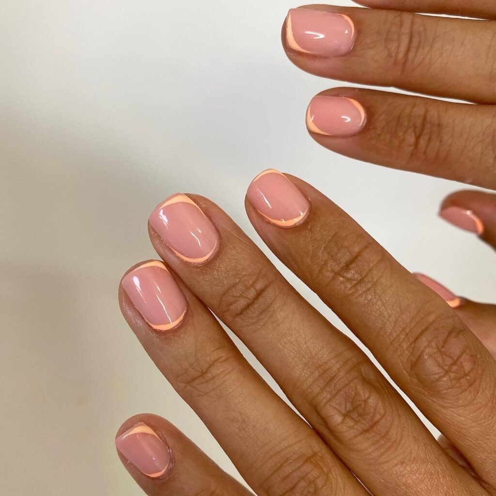 Pink manicured nails with a subtle peach outline on fingers, against a white background. Modern nail art design.