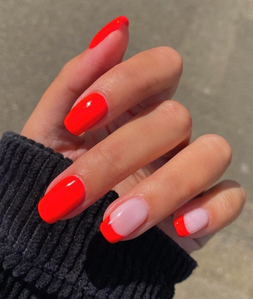 Bright orange and nude nail art design on manicured hand with sweater backdrop.