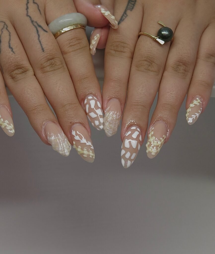 Elegant long nails with intricate white nail art and rings on fingers, showcasing trendy nail fashion.