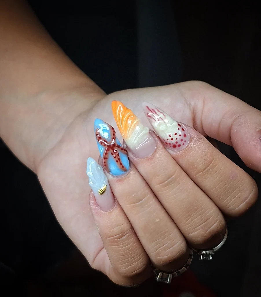 Vibrant ocean-themed nail art featuring octopus, shells, and sea patterns on stiletto-shaped nails.