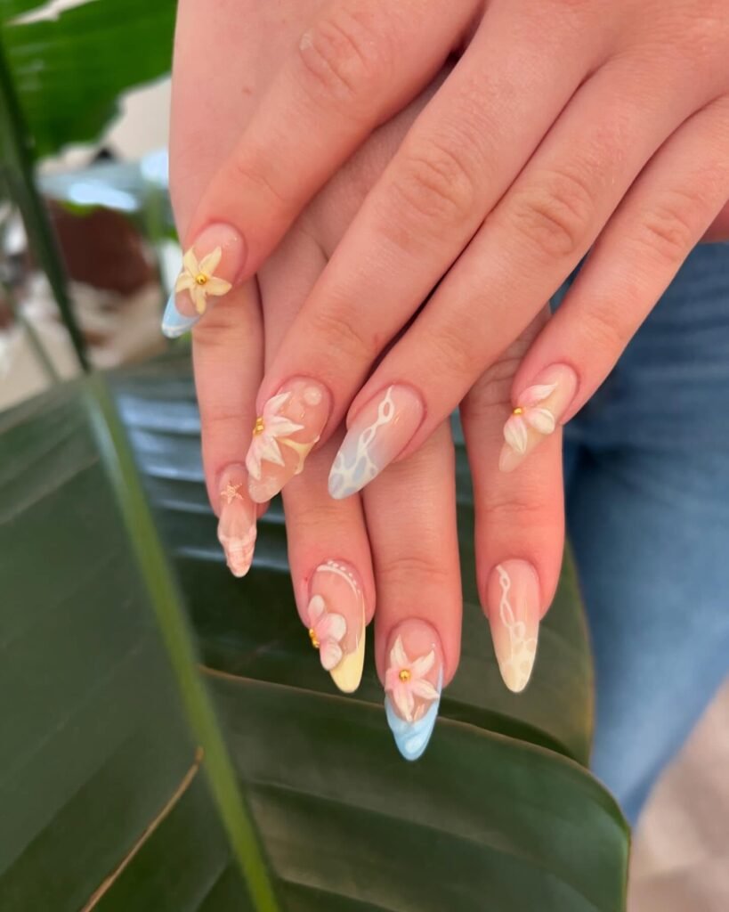 Elegant floral nail art design on long nails with pastel colors, displayed on a green leaf background.