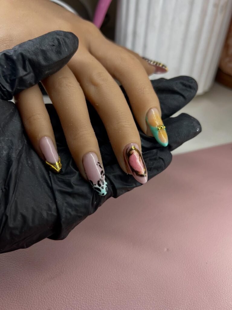 Stylish multicolored nail art with gold accents and leopard print pattern on manicured hand in black gloves.