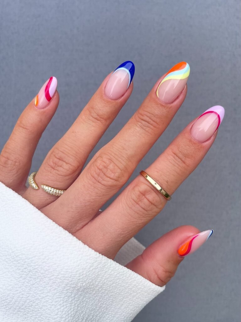 Colorful abstract nail art on an almond-shaped manicure with a white sleeve and gold rings in the background.
