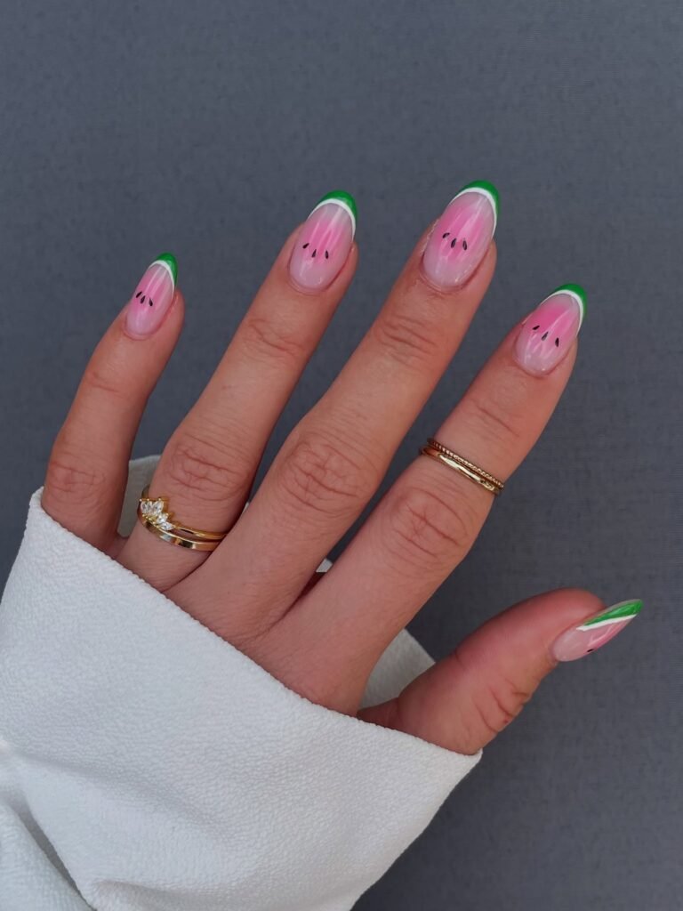 Hand with watermelon-themed nail art, featuring pink, green, and black accents against a white sleeve background.