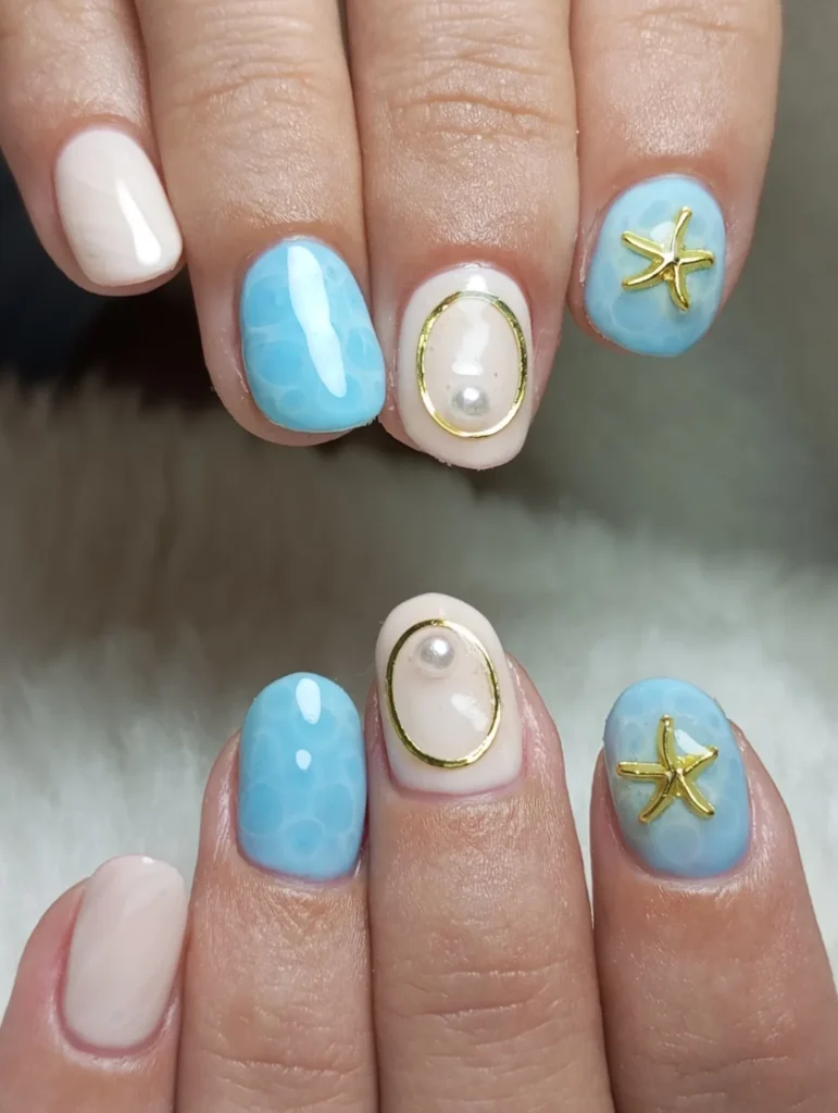 Elegant ocean-themed nail art with blue polish, starfish accents, and pearl embellishments on manicured fingers.