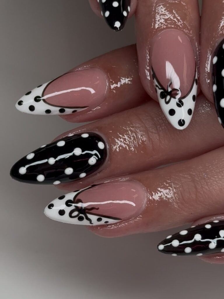 Black and white polka dot nails with bow design on glossy pink base, showcasing chic, elegant nail art.