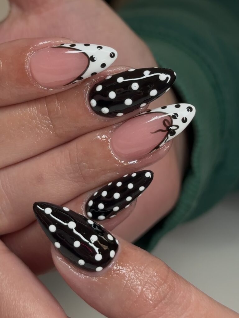 Polka dot black and white nail art on almond-shaped nails, featuring intricate patterns and shiny finish.