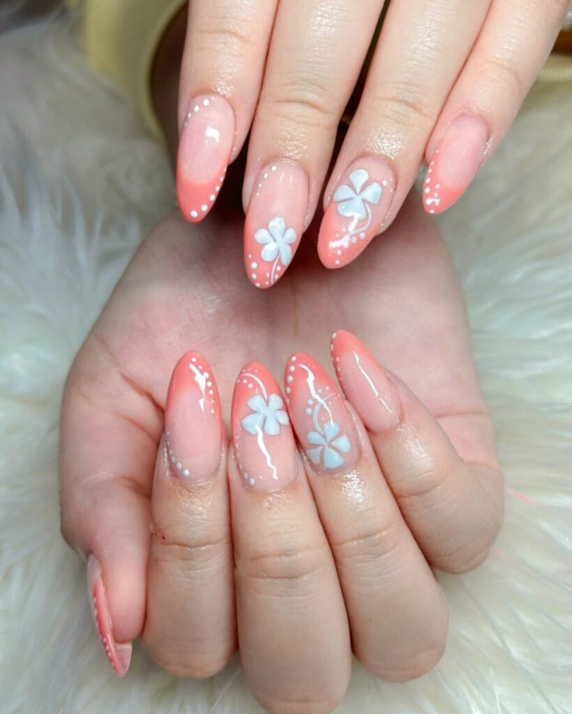 Elegant floral nail art with peach polish and white flower designs on manicured hands.