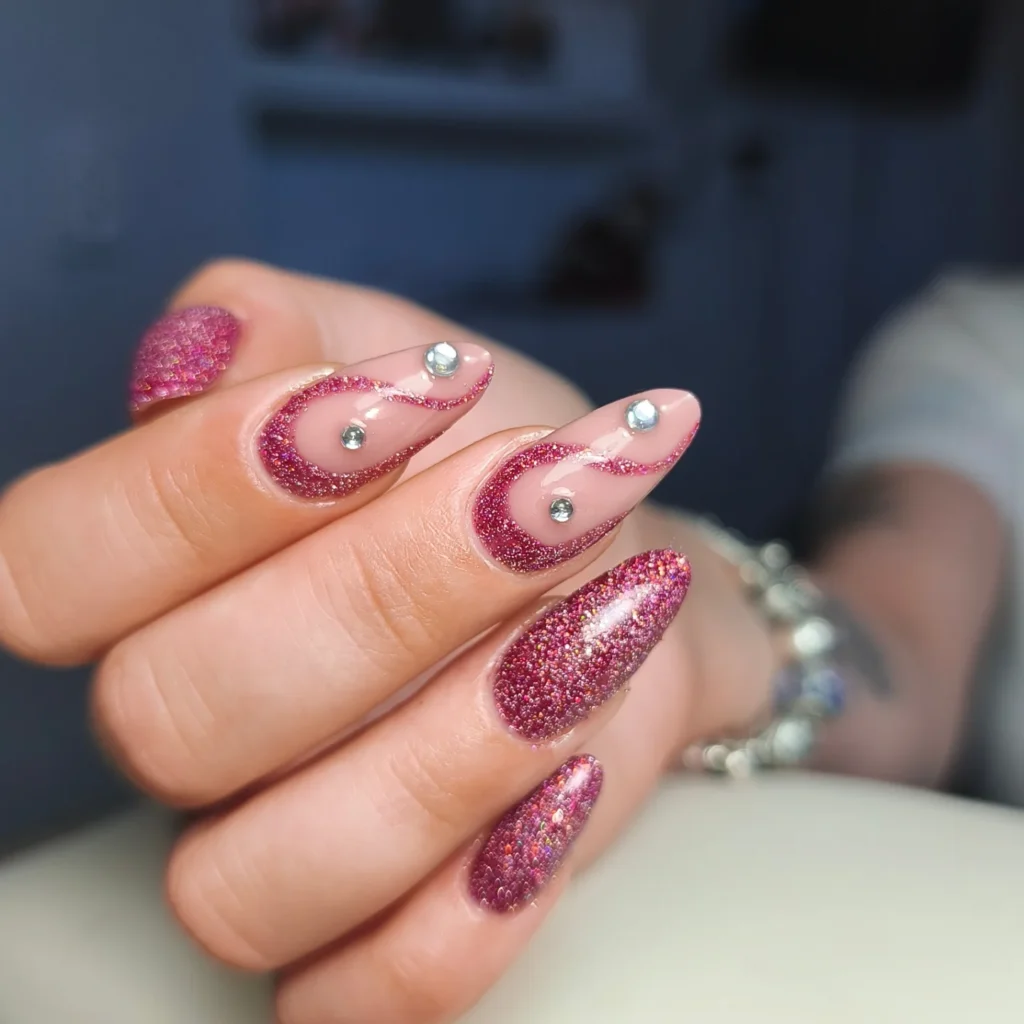 Glittery pink almond-shaped nails with rhinestone accents, showcasing intricate nail art design.
