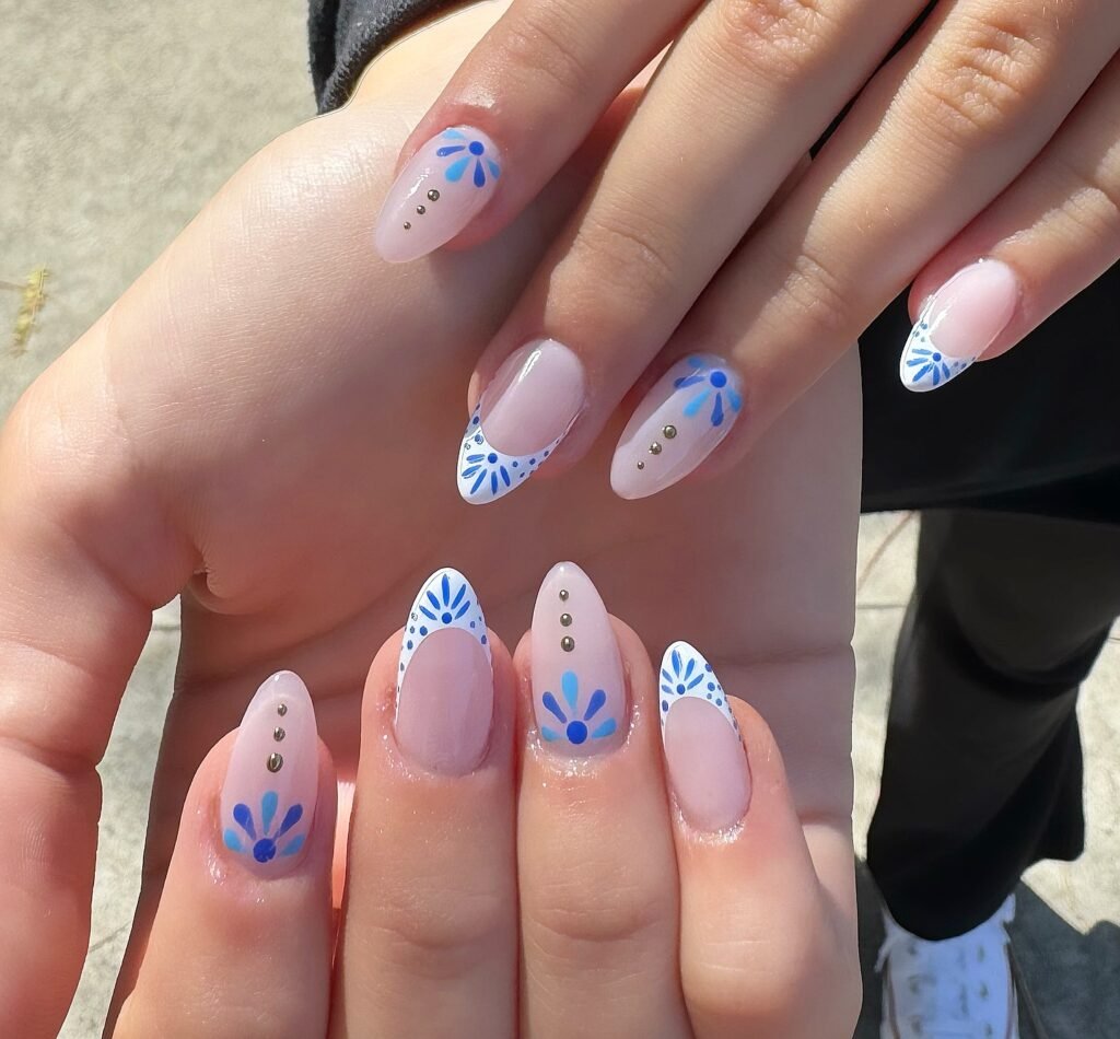 Stylish nails with blue floral designs and gold accents on a neutral background.