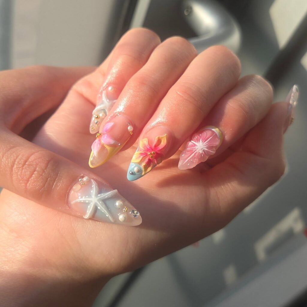Tropical-themed nail art with 3D floral designs, starfish, and pearls on almond-shaped nails in sunlight.