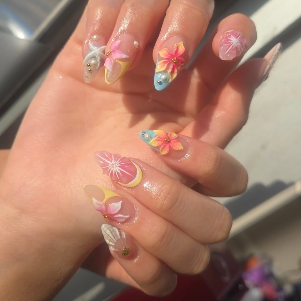 Close-up of a hand with colorful floral 3D nail art, featuring pink, yellow, and blue designs.