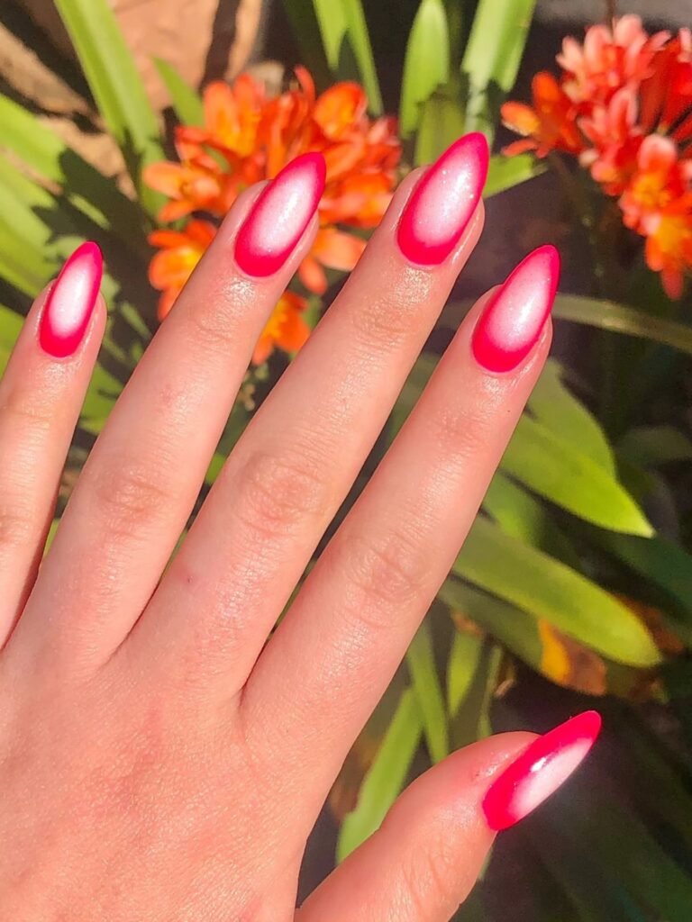 Close-up of vibrant pink and white gradient nails with orange flowers in the background.