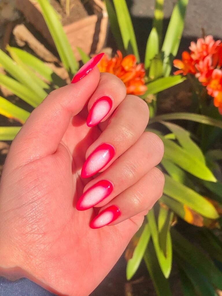 Vibrant pink and white gradient stiletto nails with a floral background in bright sunlight.