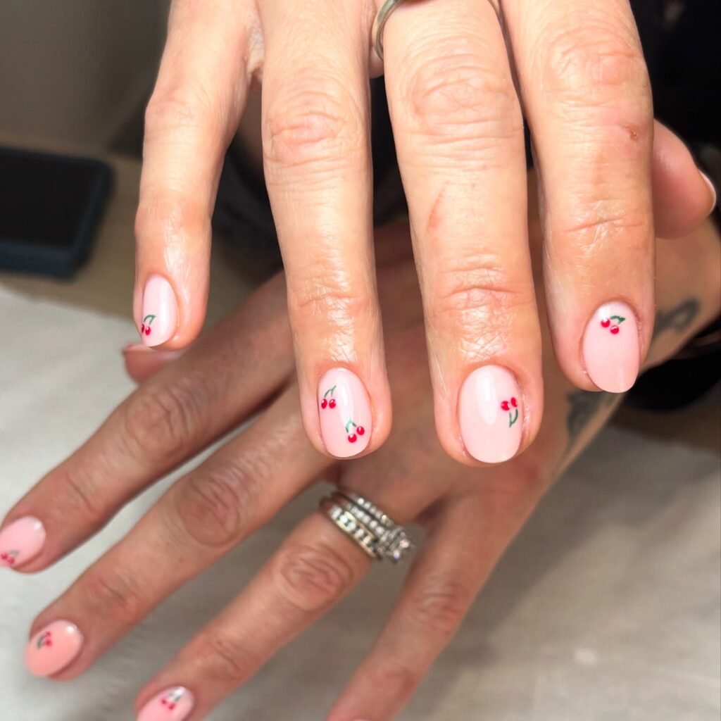Elegant cherry nail art on short nails with a light pink base, showcasing a trendy and minimal style.