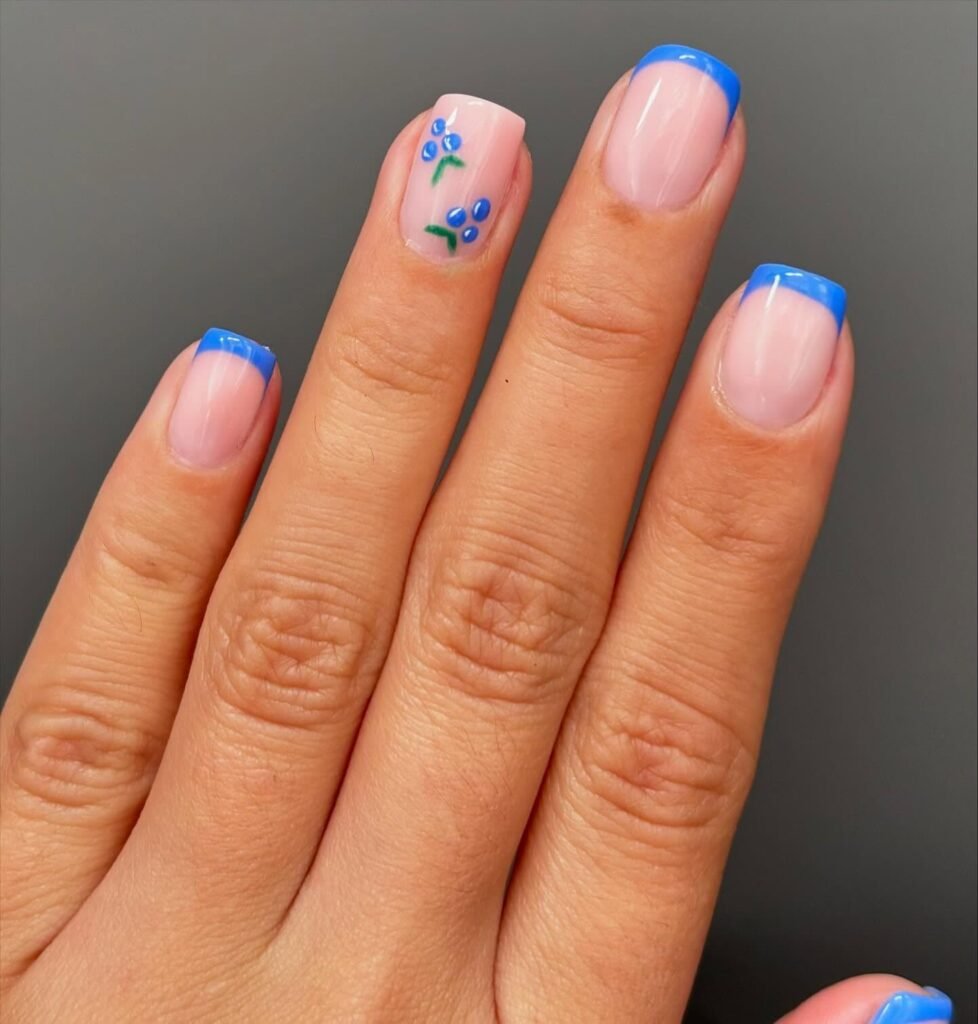 Hand with blue French manicure and floral nail art on ring finger.