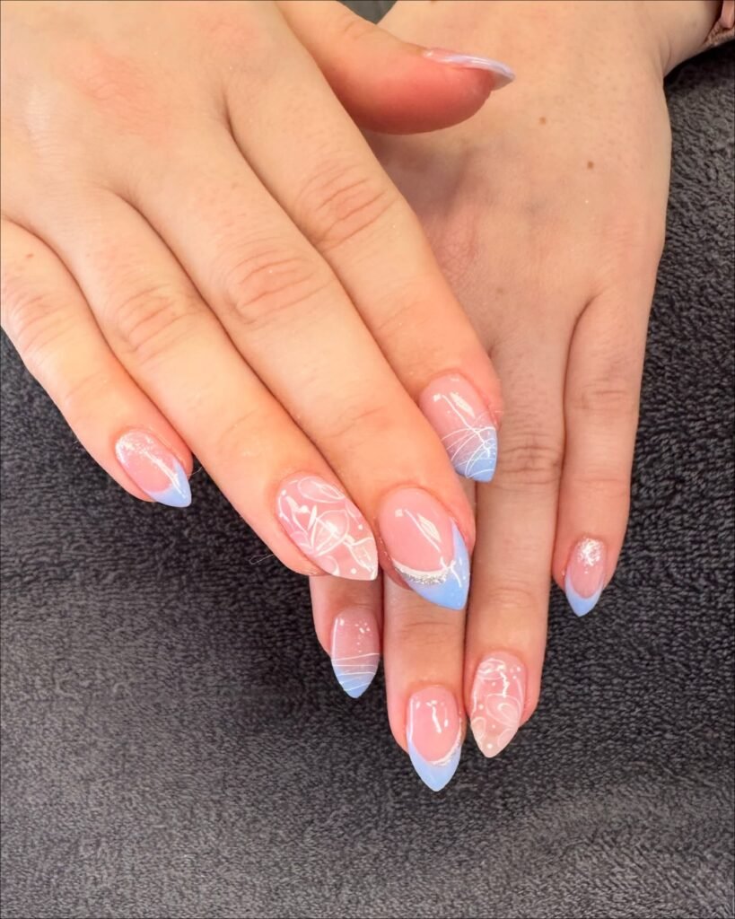 Elegant pastel blue and pink nail art with intricate white patterns, displayed on a dark textured background.