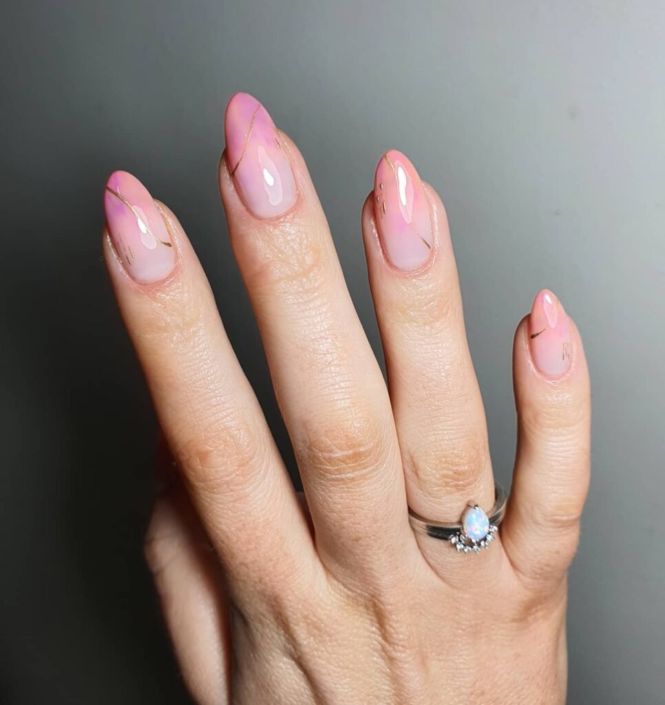 Elegant pink almond nails with gold accents and a silver ring featuring a pear-shaped opal gemstone.