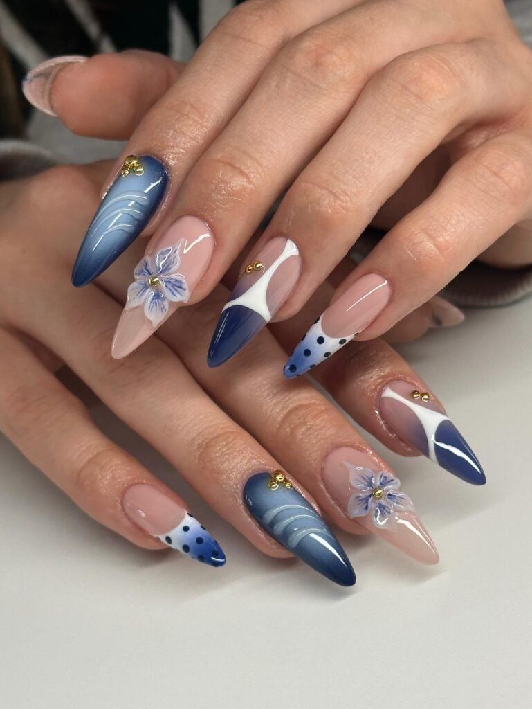 Blue and white floral nail art with intricate patterns and gold accents on almond-shaped nails.