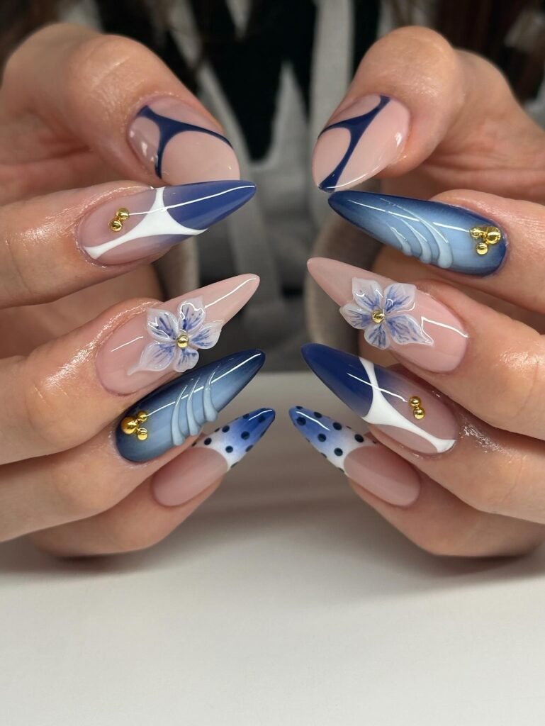Elegant blue and nude stiletto nails with 3D floral designs and gold accents, featuring geometric patterns.