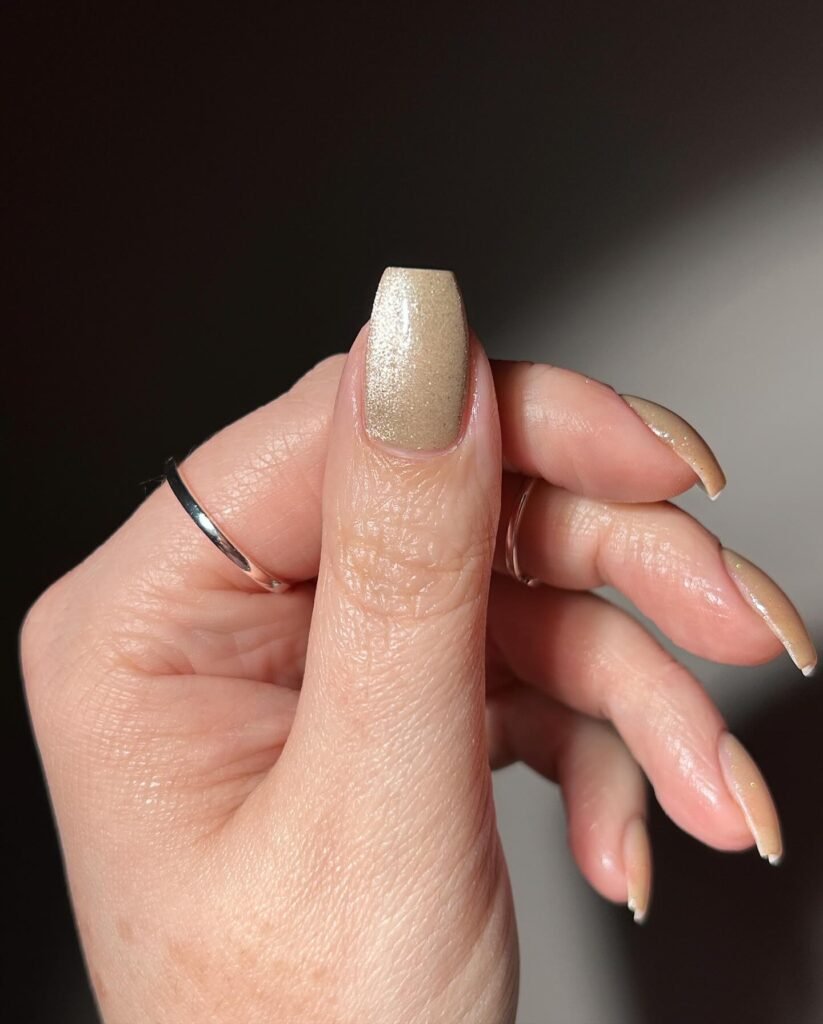 Close-up of a hand with shimmering beige nail polish and a silver ring, showcasing elegant nail art.