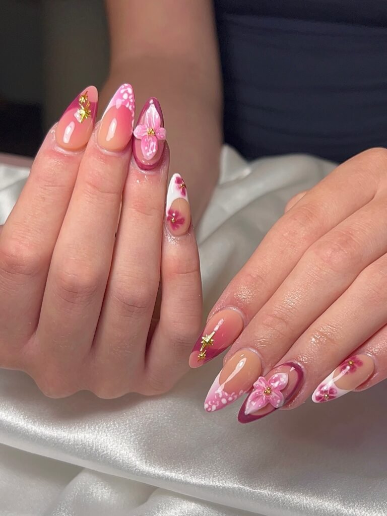 Elegant pink and white floral nail art with rhinestones on almond-shaped nails.