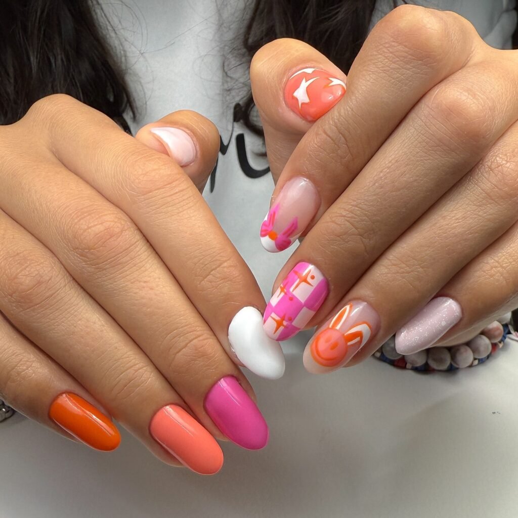 Colorful nail art with orange, pink, stars, and bunny designs on manicured hands.