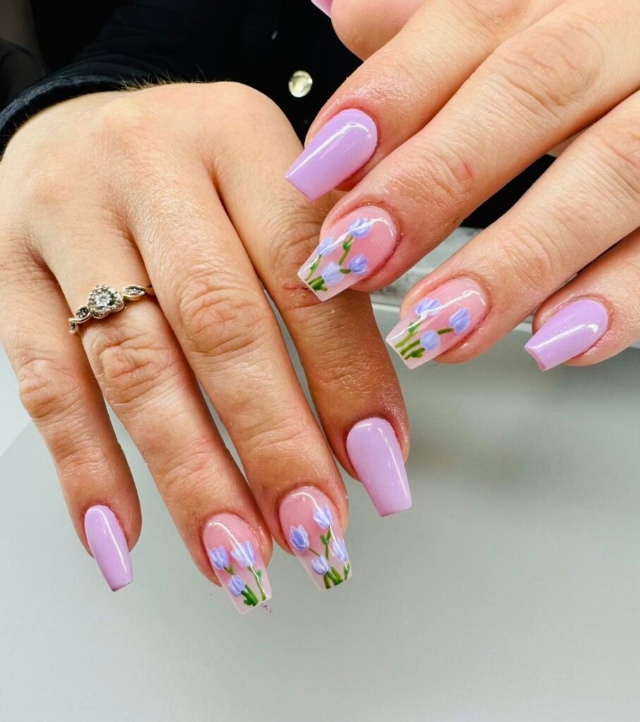 Lilac and floral nail art design on manicured hands with ring; pastel purple nails, delicate flower pattern.