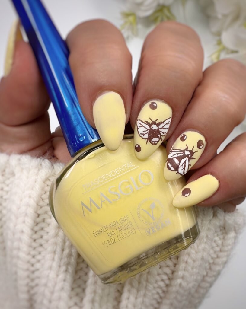 Yellow nail polish with bee designs on nails. Masglo vegan nail lacquer in a person's hand. Summer nail art.