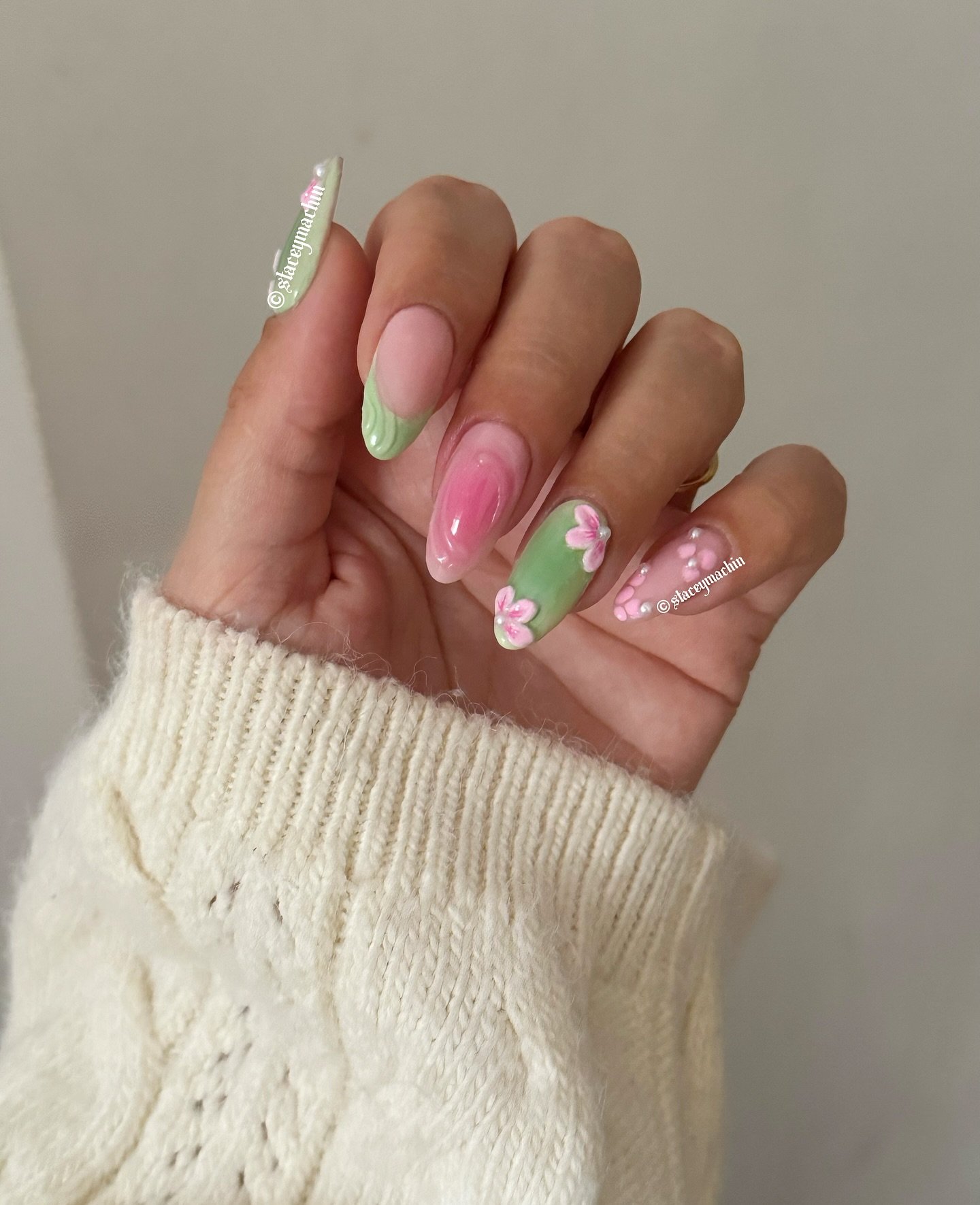 Pastel green and pink floral nail art with 3D flowers and a cozy cream sweater sleeve.