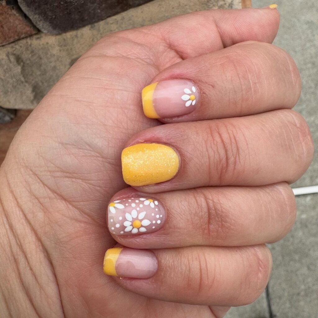 Yellow and floral nail art design on fingertips, featuring daisy patterns and a bright yellow polish.
