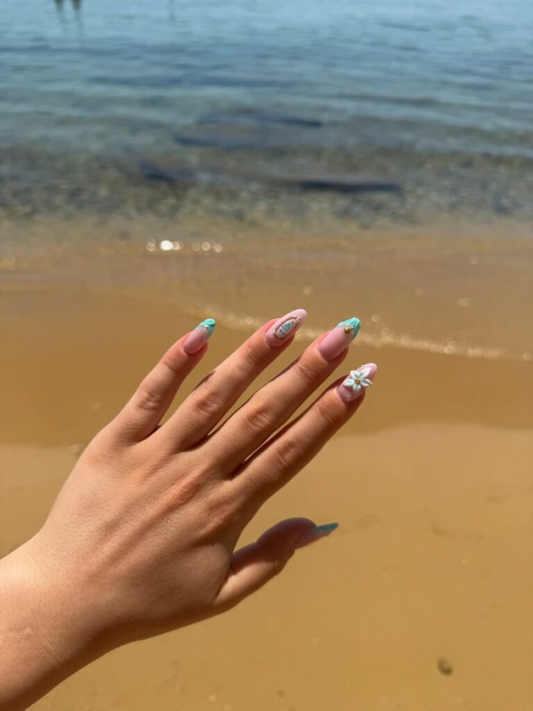 Hand with floral nail art displayed against a sandy beach and ocean background.