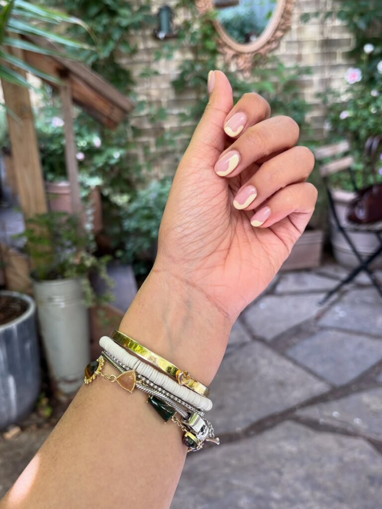 Hand with stylish bracelets and pastel nail art, set against a garden backdrop.