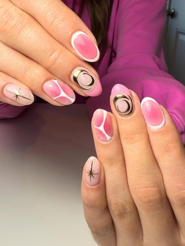 Pink and gold galaxy-themed nail art design with shimmering accents and celestial symbols on well-manicured nails.