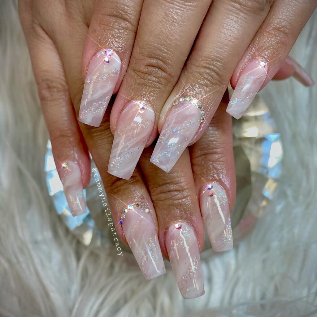 Elegant pink marble coffin nails with glitter and rhinestone accents on a furry white background.