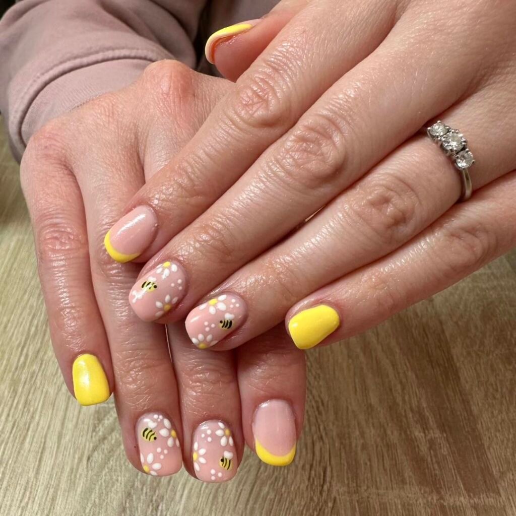 Yellow and floral bee nail art with daisy designs on a wooden surface.