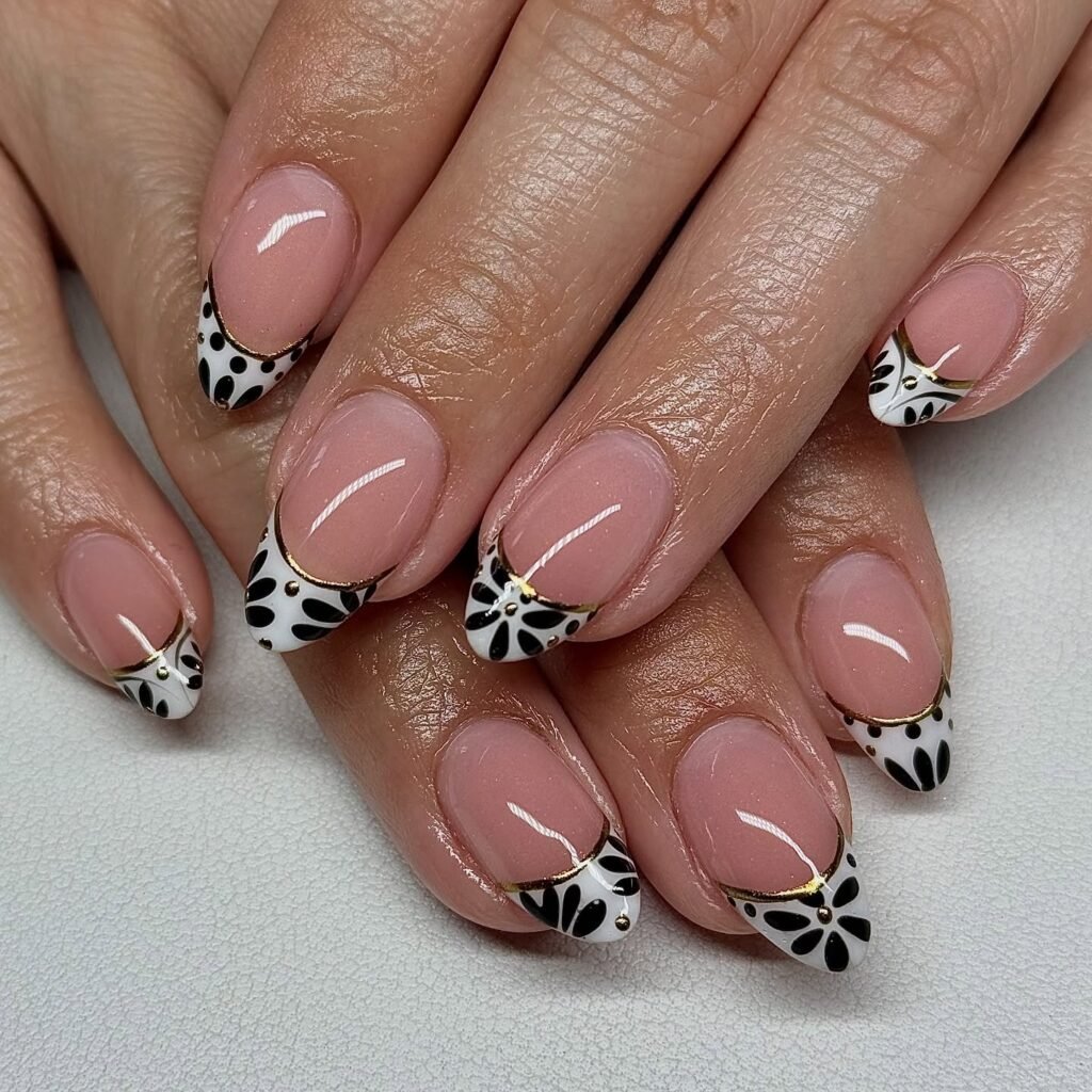Stylish black and white floral nail art with gold accents on oval nails.