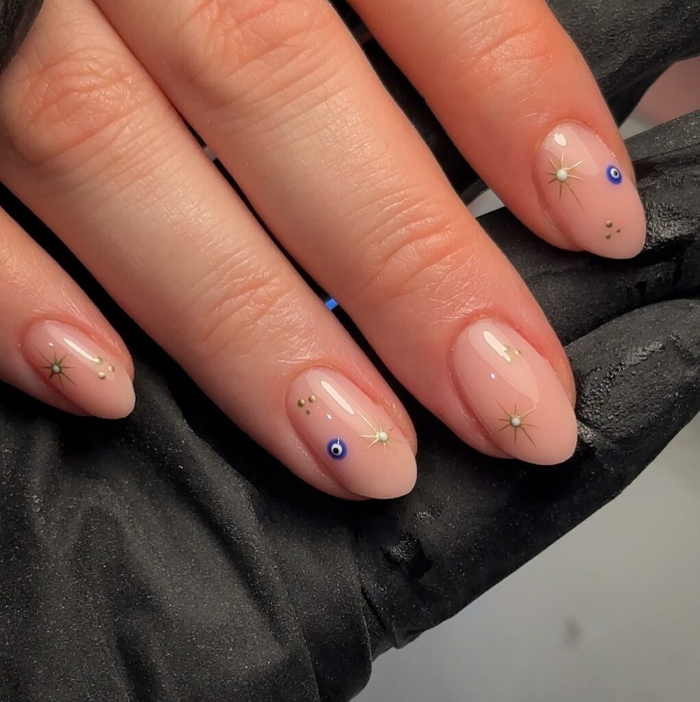 Elegant nail art with celestial and evil eye designs on nude polish, held by a gloved hand.