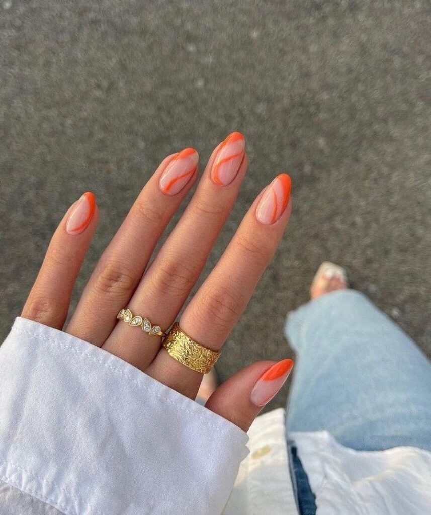 Orange gradient nail art with two gold rings on hand, white cuff and jeans in background. Stylish manicure.