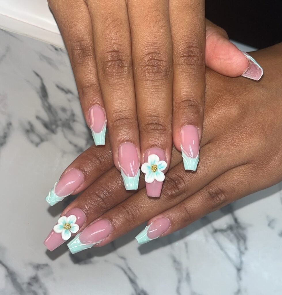 Pink and mint green French tip nails with white floral accents on a marble background.