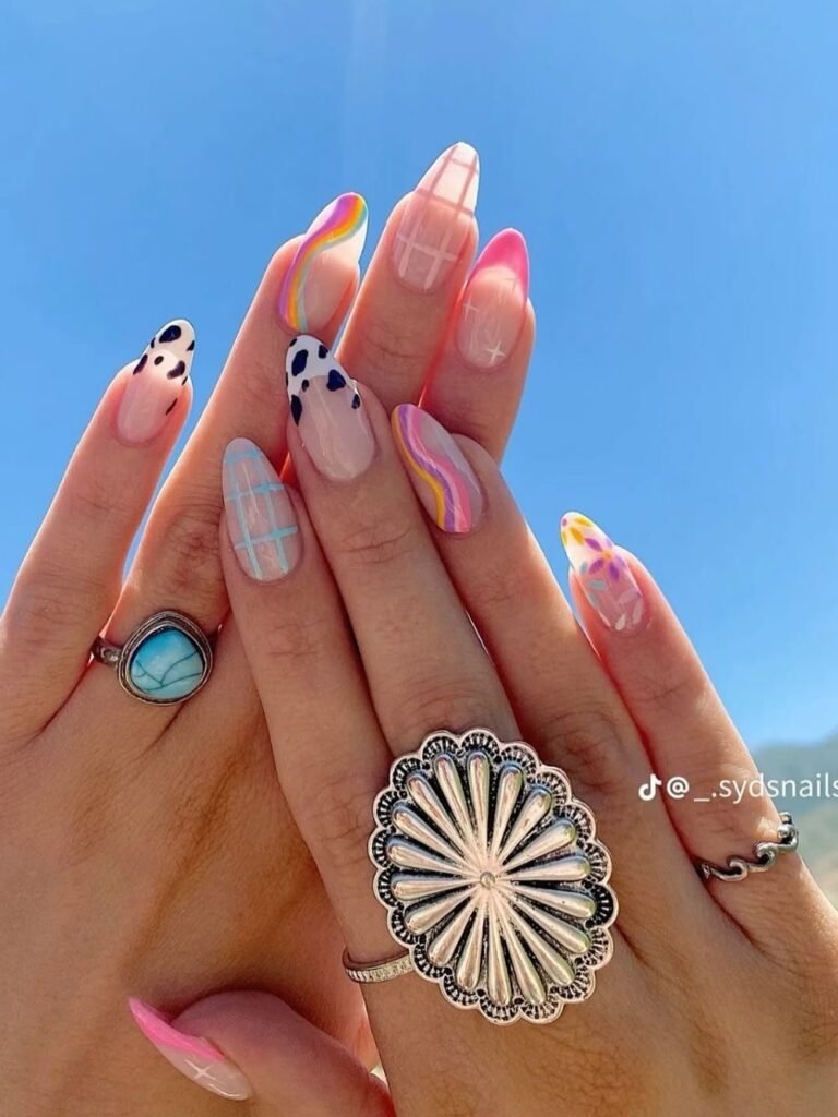 Colorful nail art designs, hands with stylish rings under a clear blue sky.
