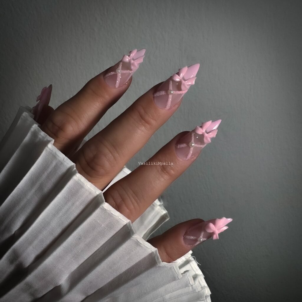 Pink 3D bow nail art on stiletto nails, paired with a white pleated sleeve.